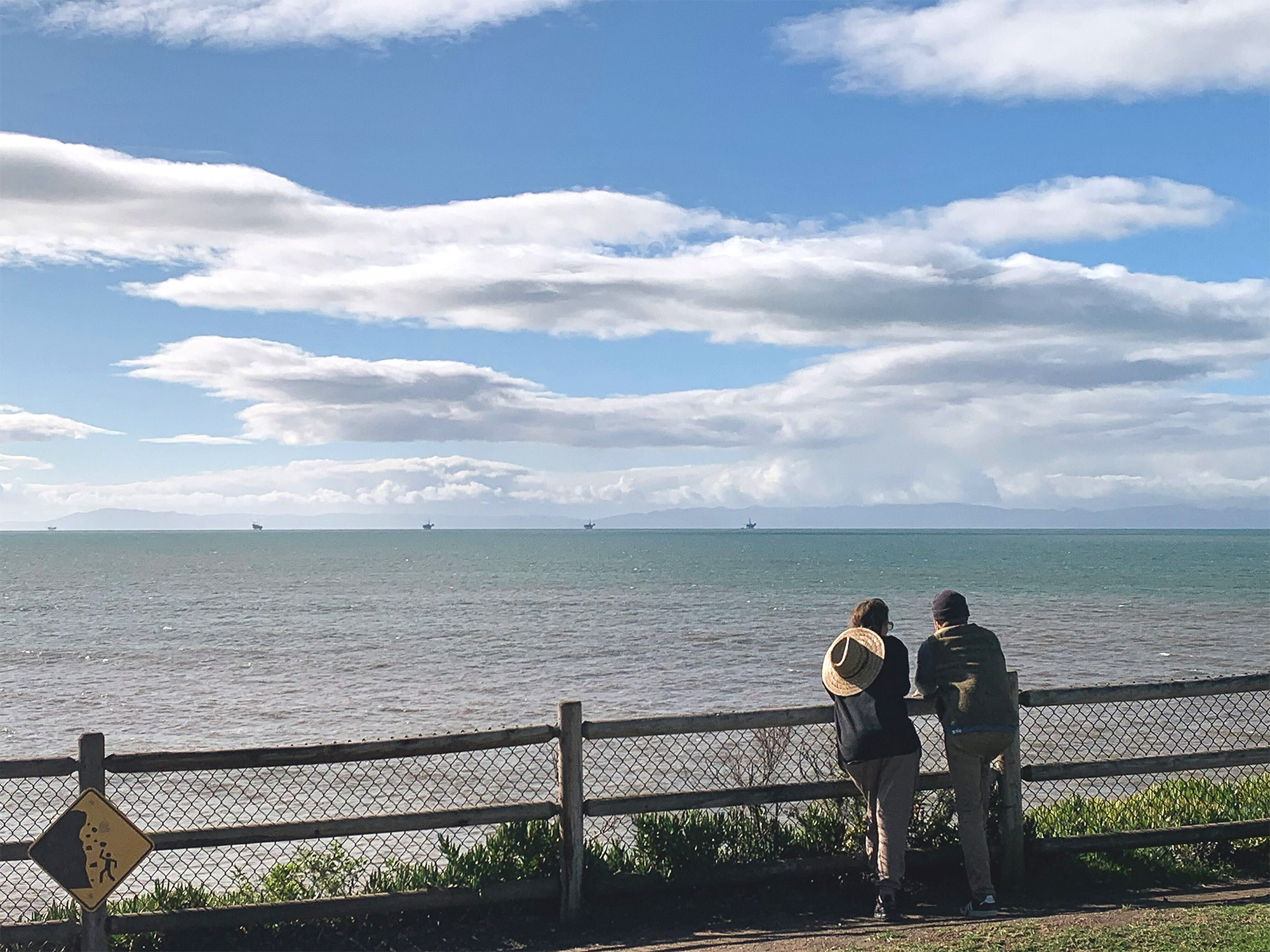 Offshore oil platforms dot the horizon as a couple looks on at California’s Summerland Beach.